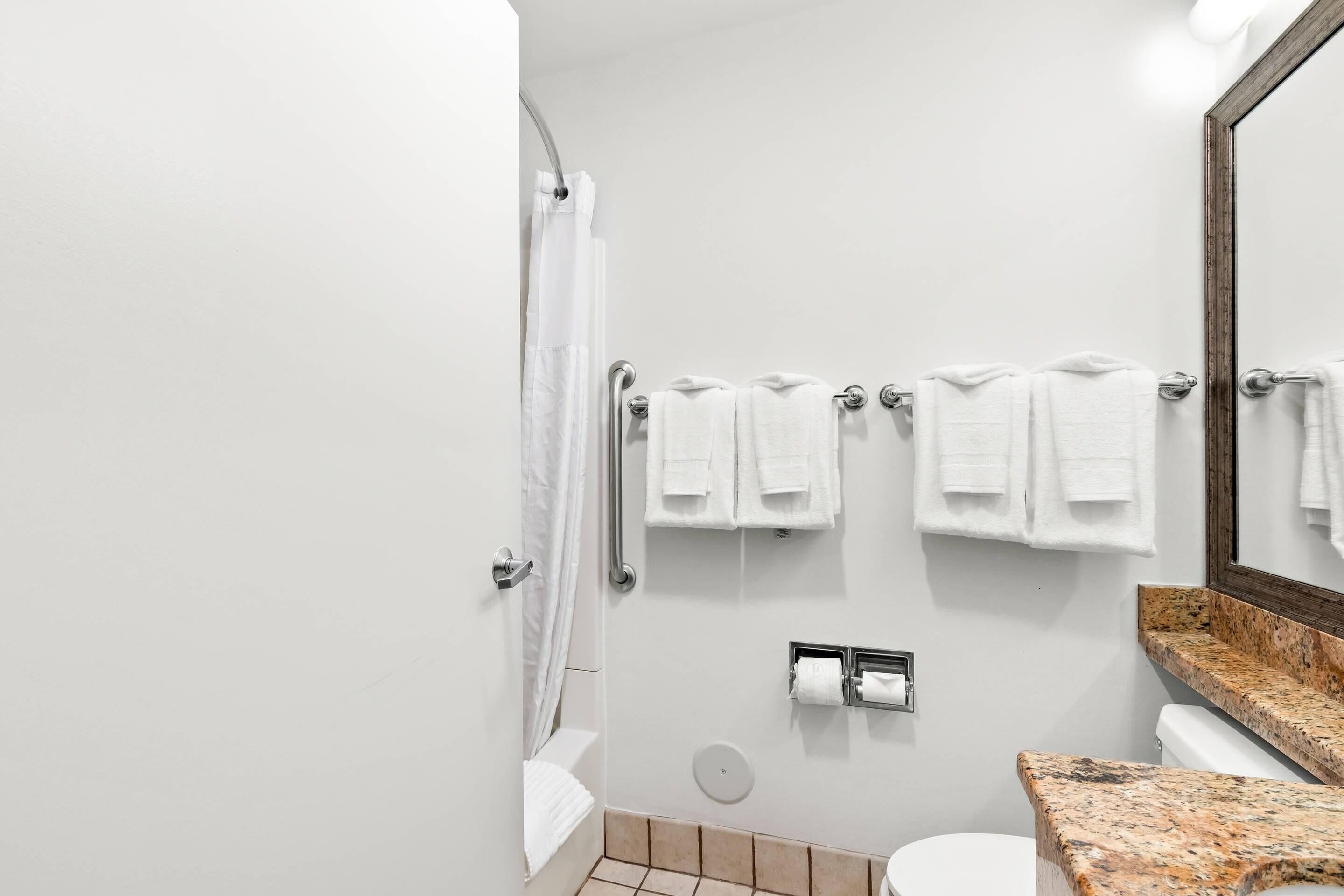 A bathroom with a shower, toilet, and a towel rack with multiple towels.