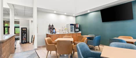 Un intérieur moderne comprenant un coin salon, un espace dédié au café et un grand téléviseur à écran plat fixé au mur.
