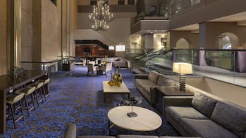 A spacious lobby with a blue patterned carpet, a chandelier, seating areas, and a staircase.