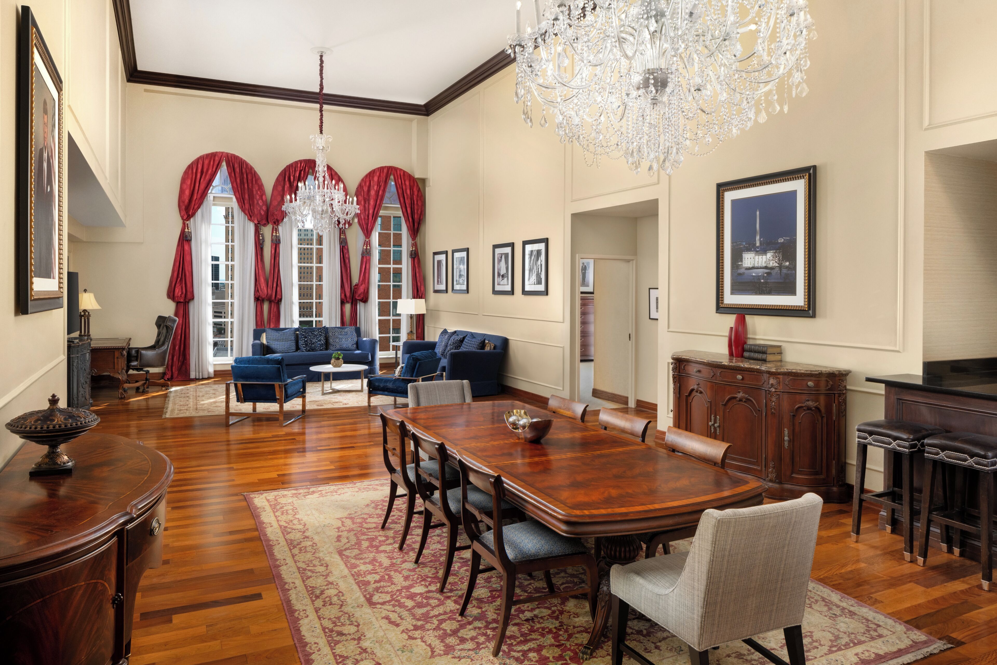 A spacious living room with a large wooden dining table, blue sofas, and a chandelier.