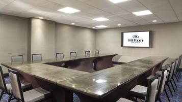 A conference room with a long table, chairs, and a screen displaying 'Hilton Fort Worth'.