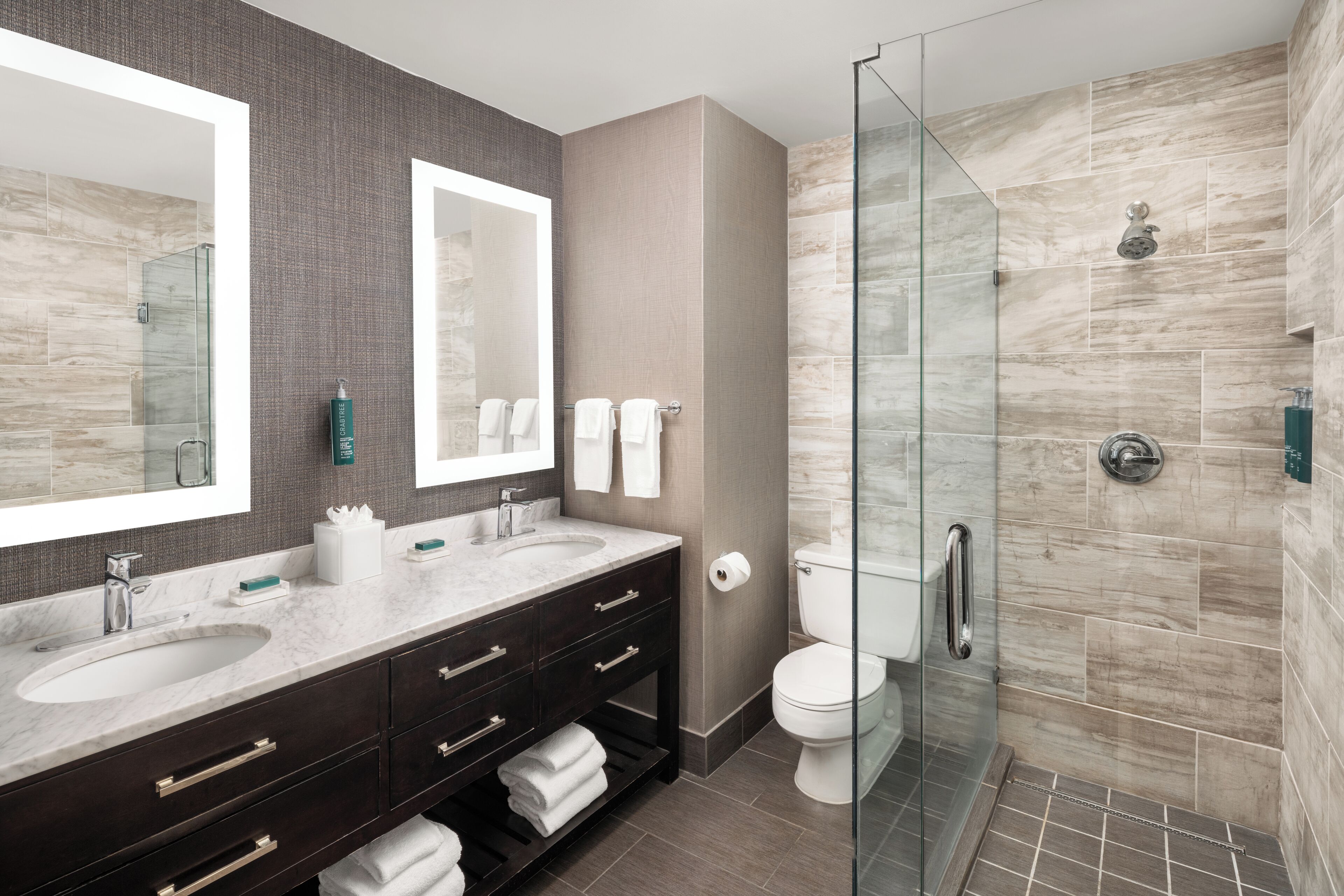 A modern bathroom with two sinks, dark wood vanity, glass shower enclosure, and a large mirror.