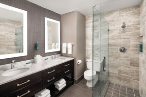 Un bagno moderno con due lavabi, mobile vanità in legno scuro, cabina doccia in vetro e uno specchio grande.