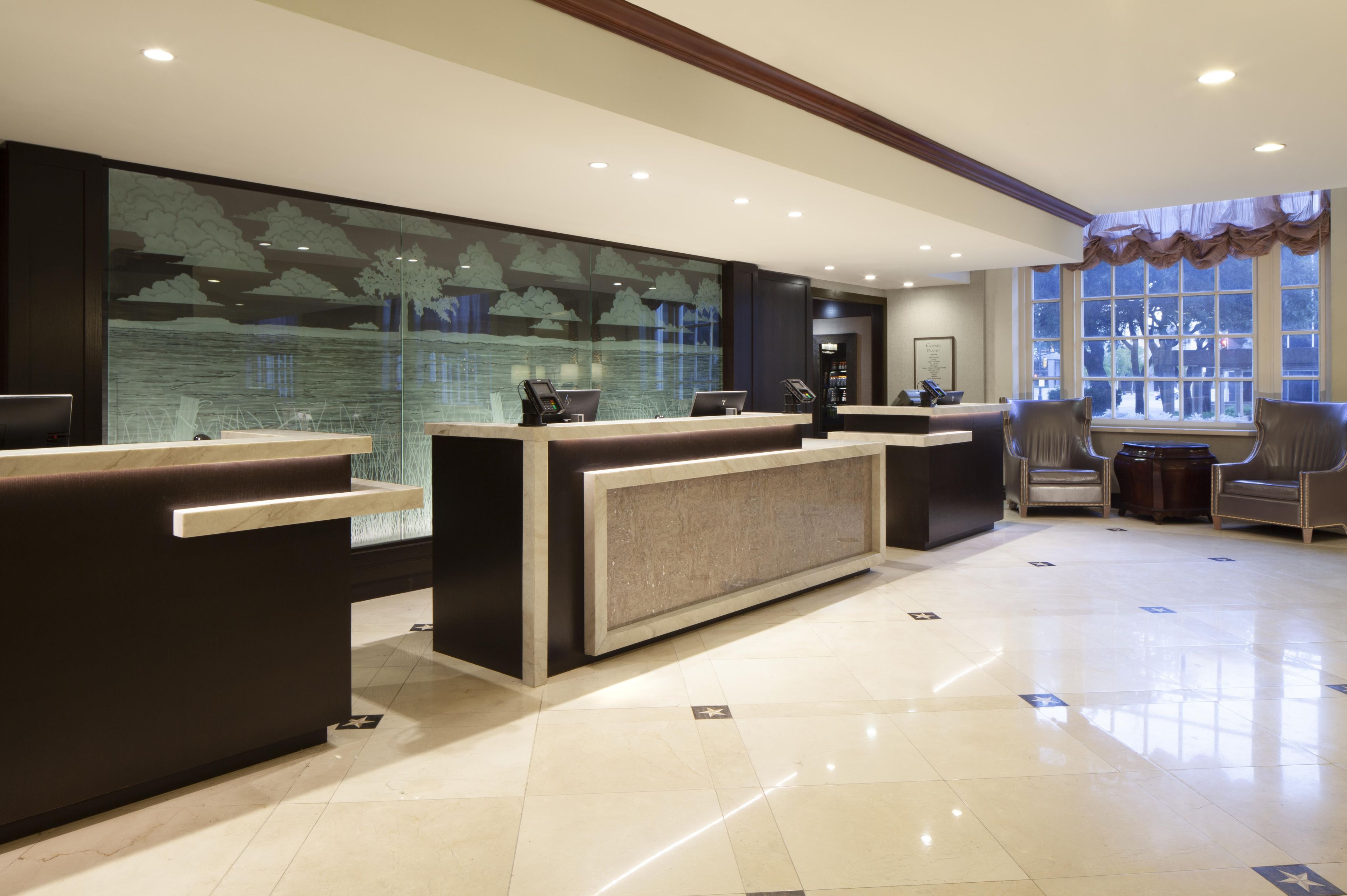 A hotel reception area with a large window, a reception desk, and a seating area with chairs.