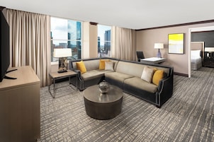 Habitación de hotel con sofá modular, una mesa redonda de centro, escritorio con lámpara y cama.