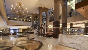 A spacious lobby with a grand chandelier, a marble reception desk, and a modern staircase. - Hilton Fort Worth (Fort Worth)