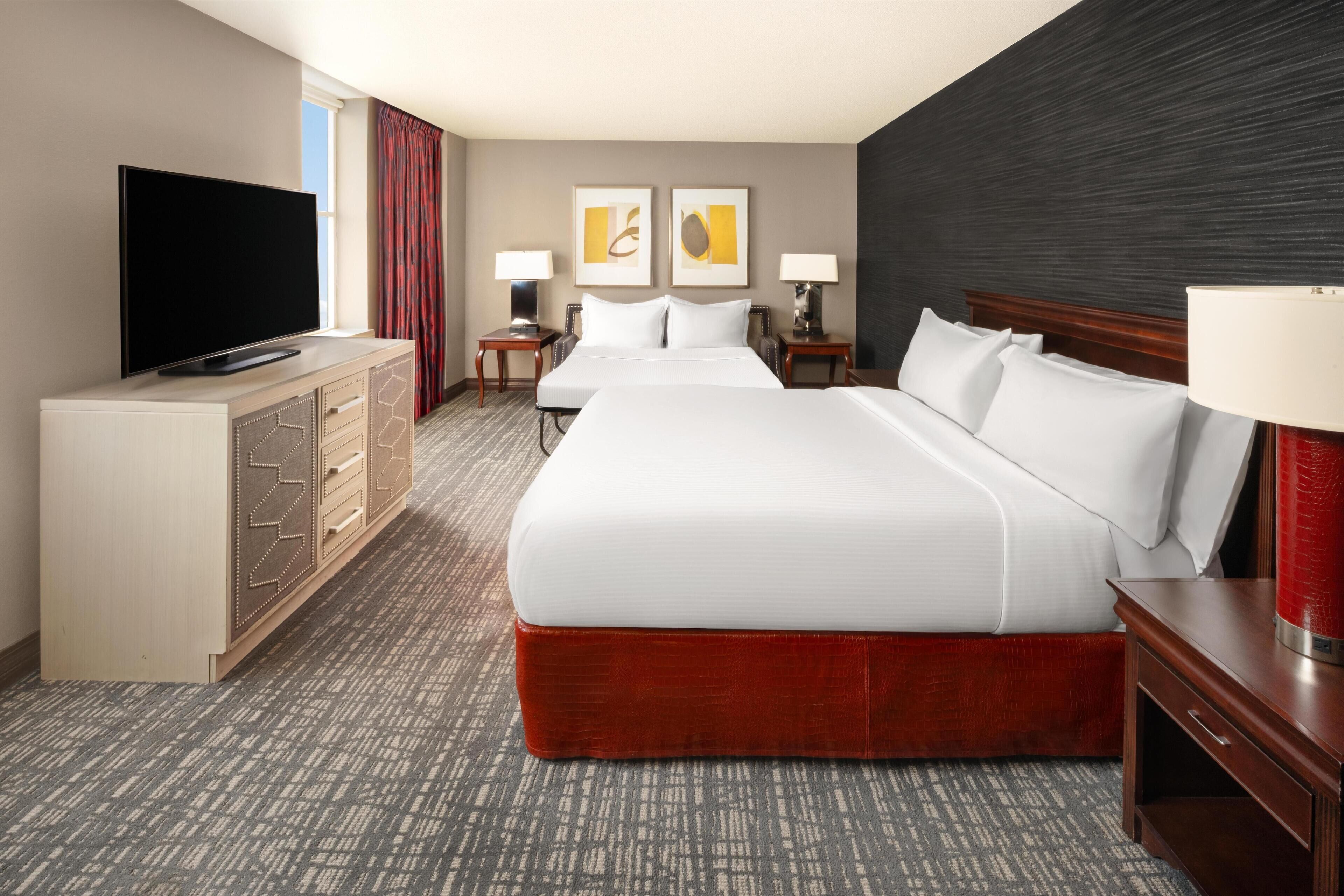 A hotel room with a large bed, a TV, a desk, and a dresser.