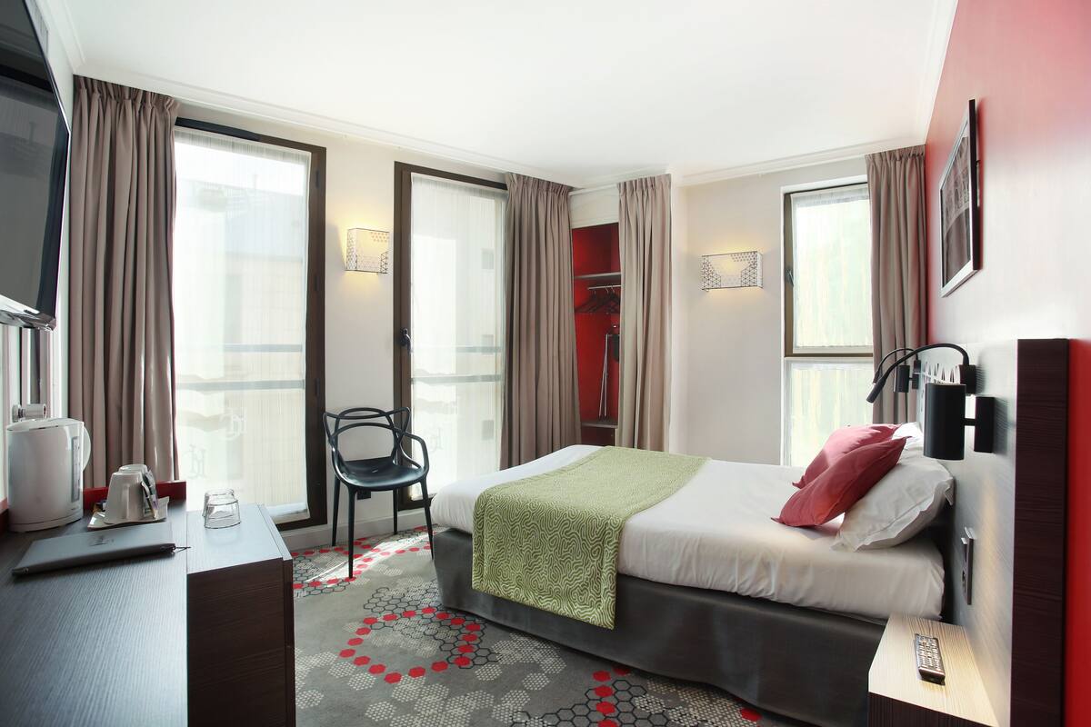 Quarto de hotel com cama, escrivaninha com cafeteira, cadeira e armário.