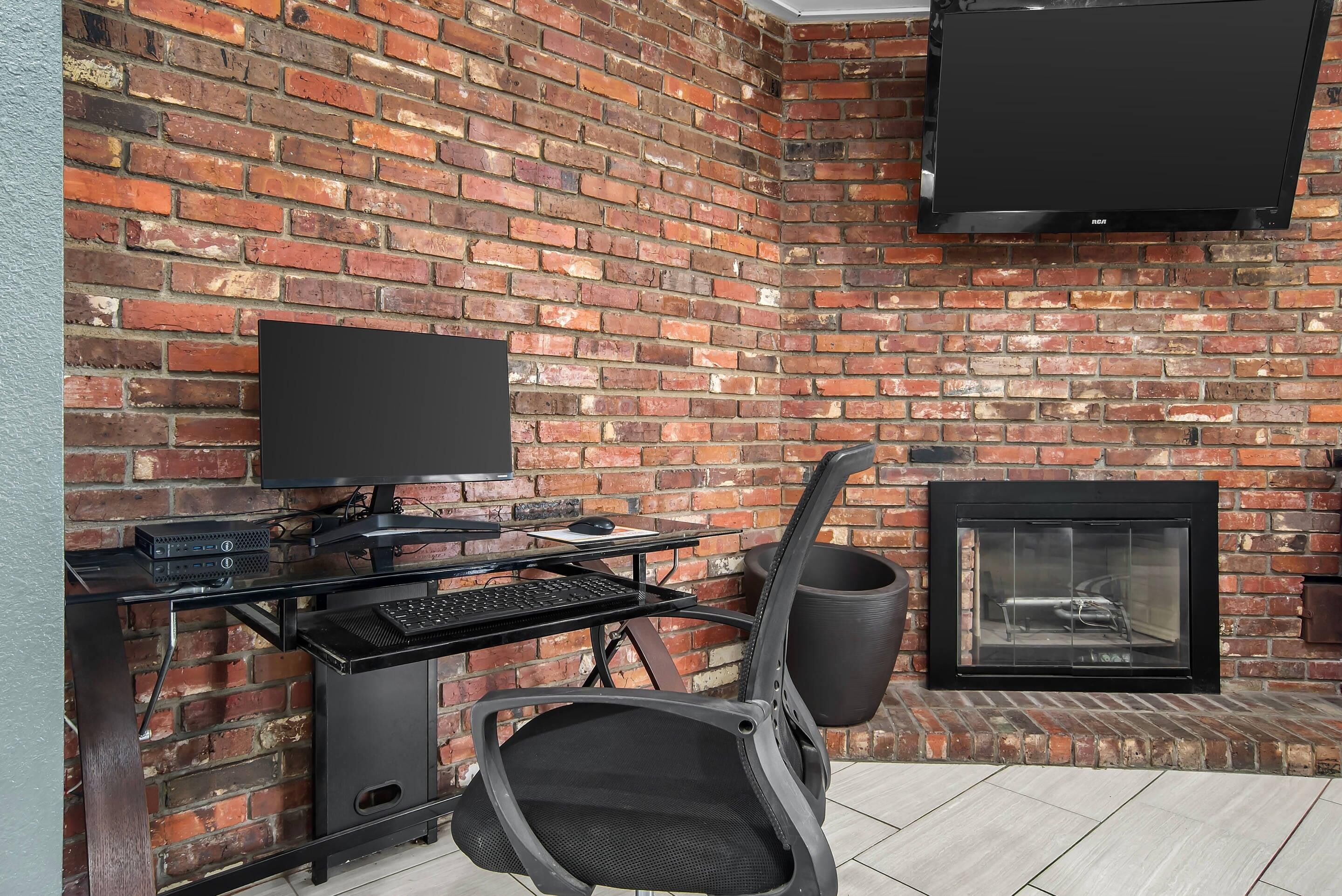 A brick wall with a flat-screen TV mounted above a computer desk.
