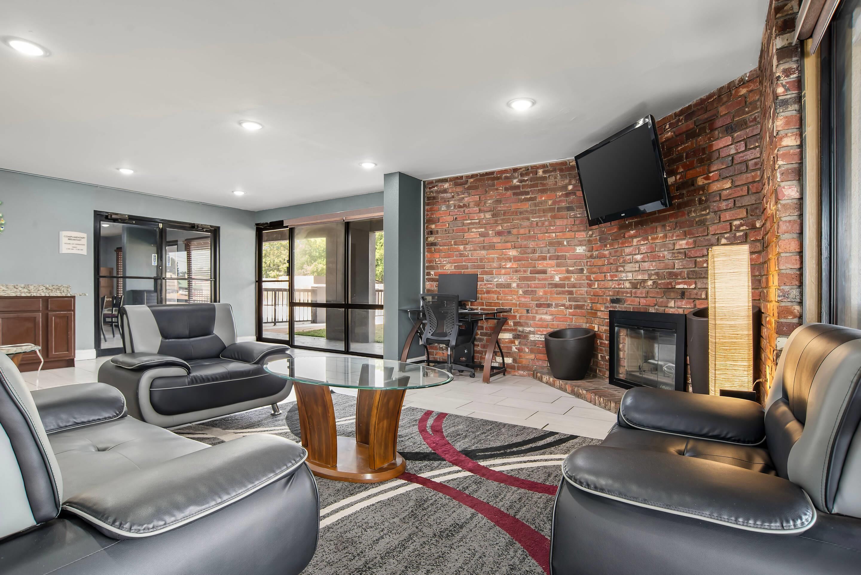 A modern lounge area with leather sofas, a glass-top coffee table, and a brick wall with a fireplace.