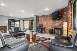 A modern lounge area with leather sofas, a glass-top coffee table, and a brick wall with a fireplace.