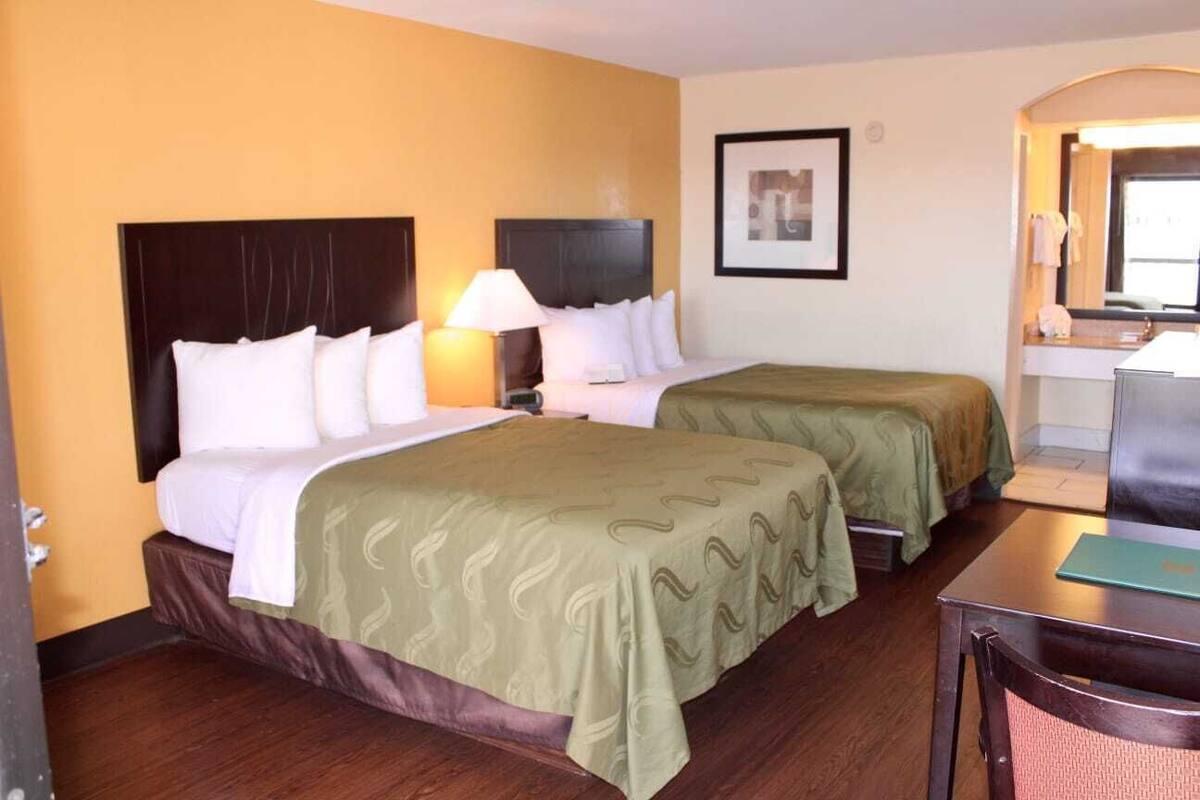 Een hotelkamer met twee bedden, een bureau, een stoel, een spiegel en een ingelijst schilderij aan de muur.
