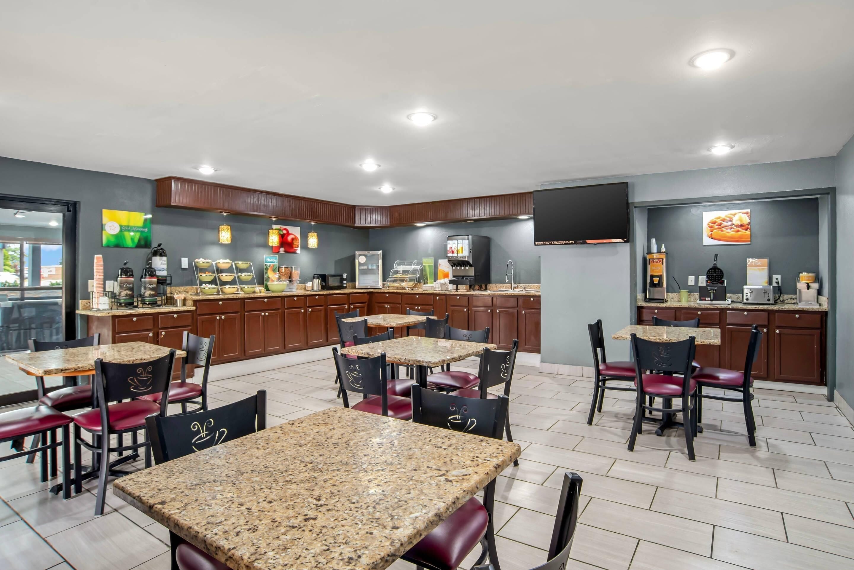 A modern kitchen with granite countertops, a coffee station, and a dining area with chairs and tables.