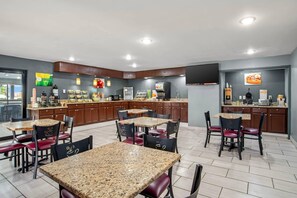 A modern kitchen with granite countertops, a coffee station, and a dining area with chairs and tables.