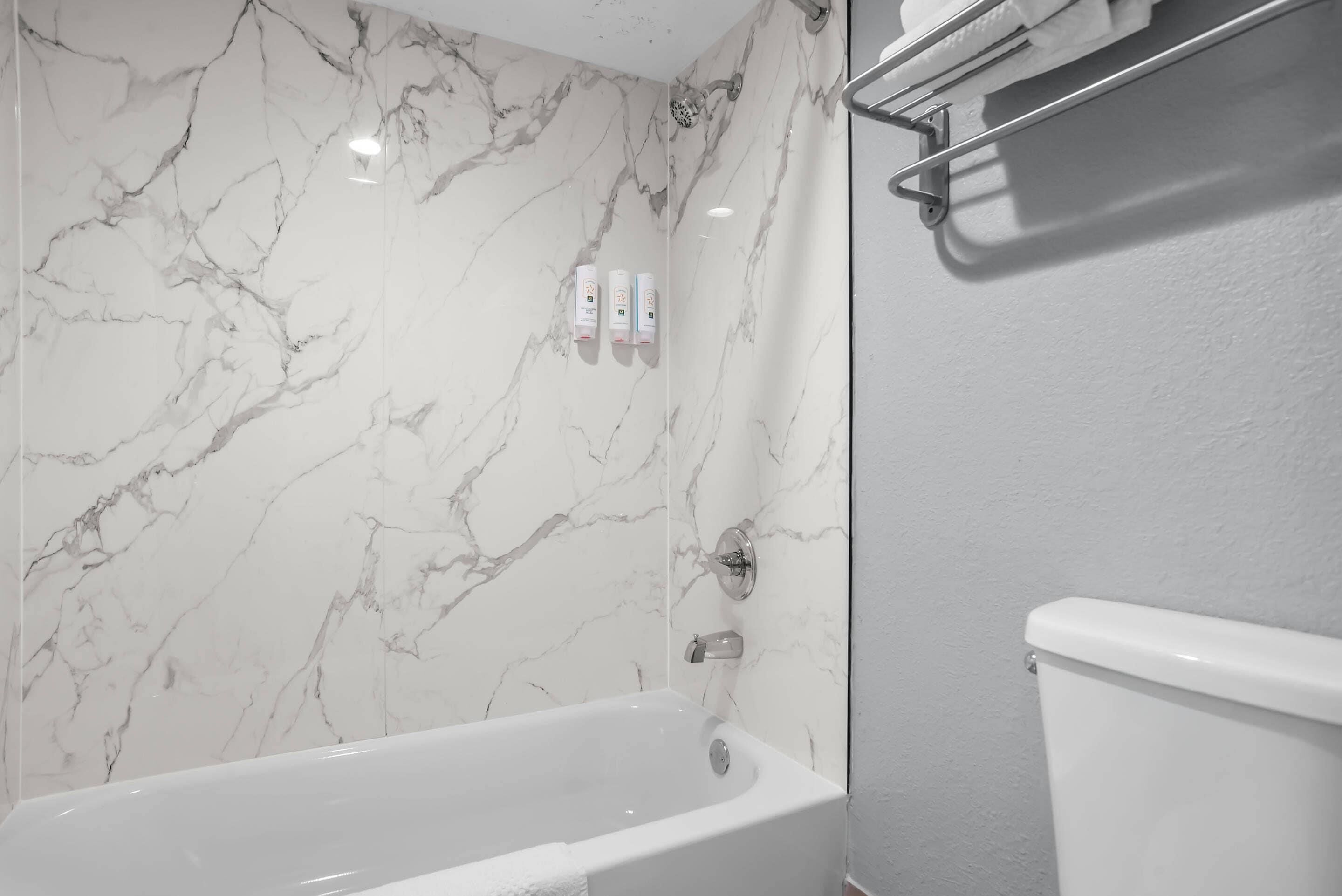Un baño con una bañera blanca, paredes de mármol y un inodoro.