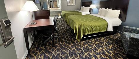 A hotel room with two beds, a desk, a chair, and a bathroom.