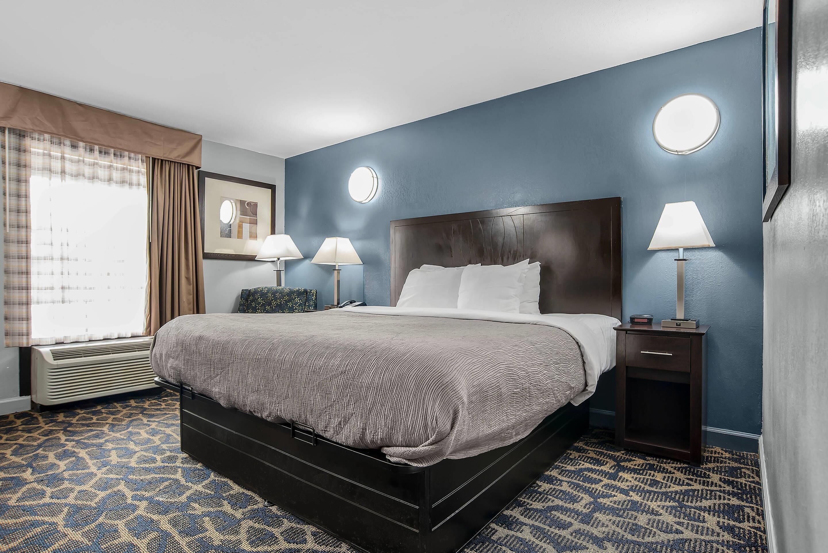Ein Hotelzimmer mit einem großen Bett, zwei Nachttischlampen, einem runden Spiegel und einem Fenster mit Vorhängen.