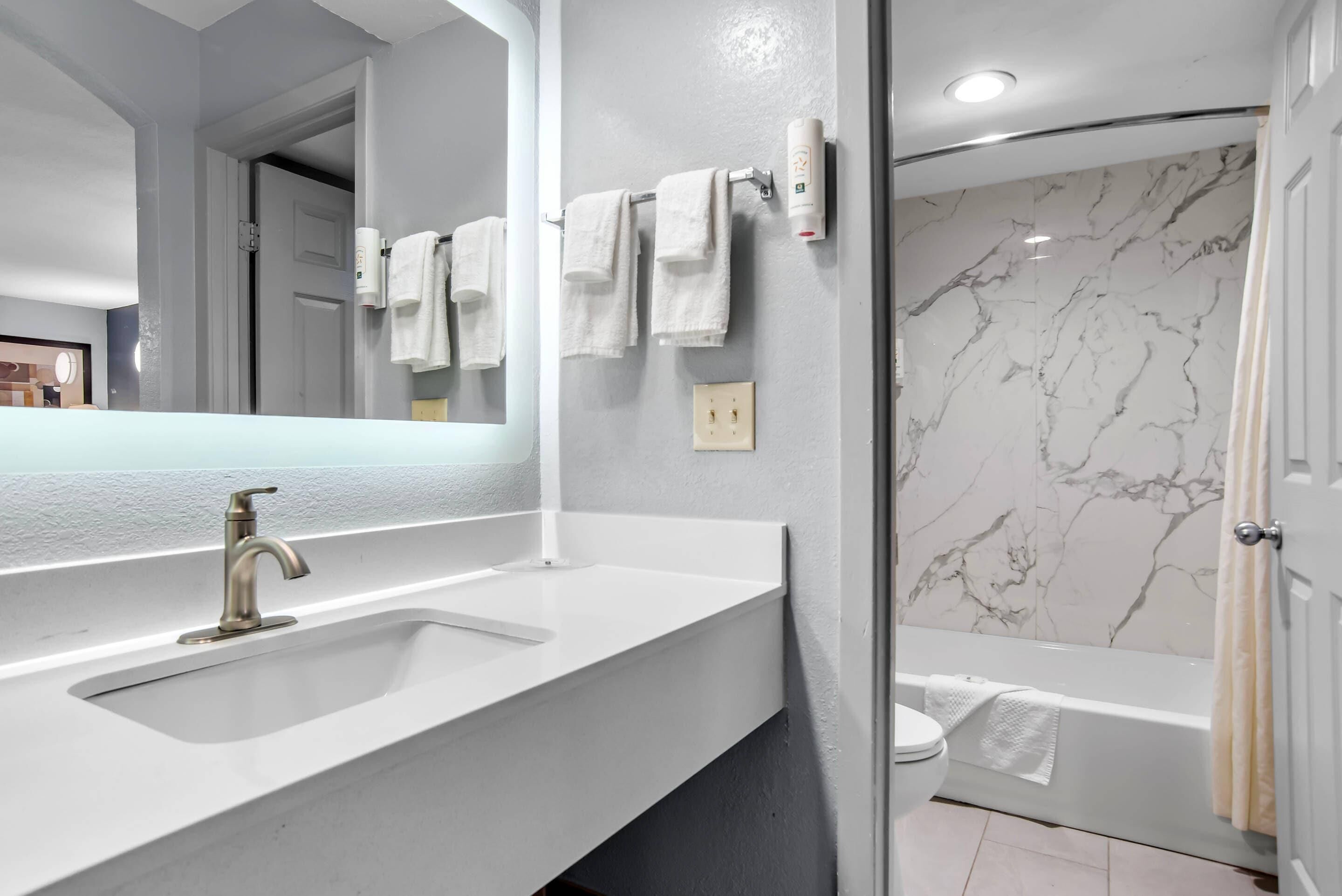 Un baño con lavamanos blanco, un espejo, toallero y ducha con paredes de mármol.