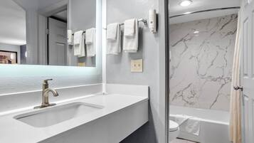Un baño con lavamanos blanco, un espejo, toallero y ducha con paredes de mármol.