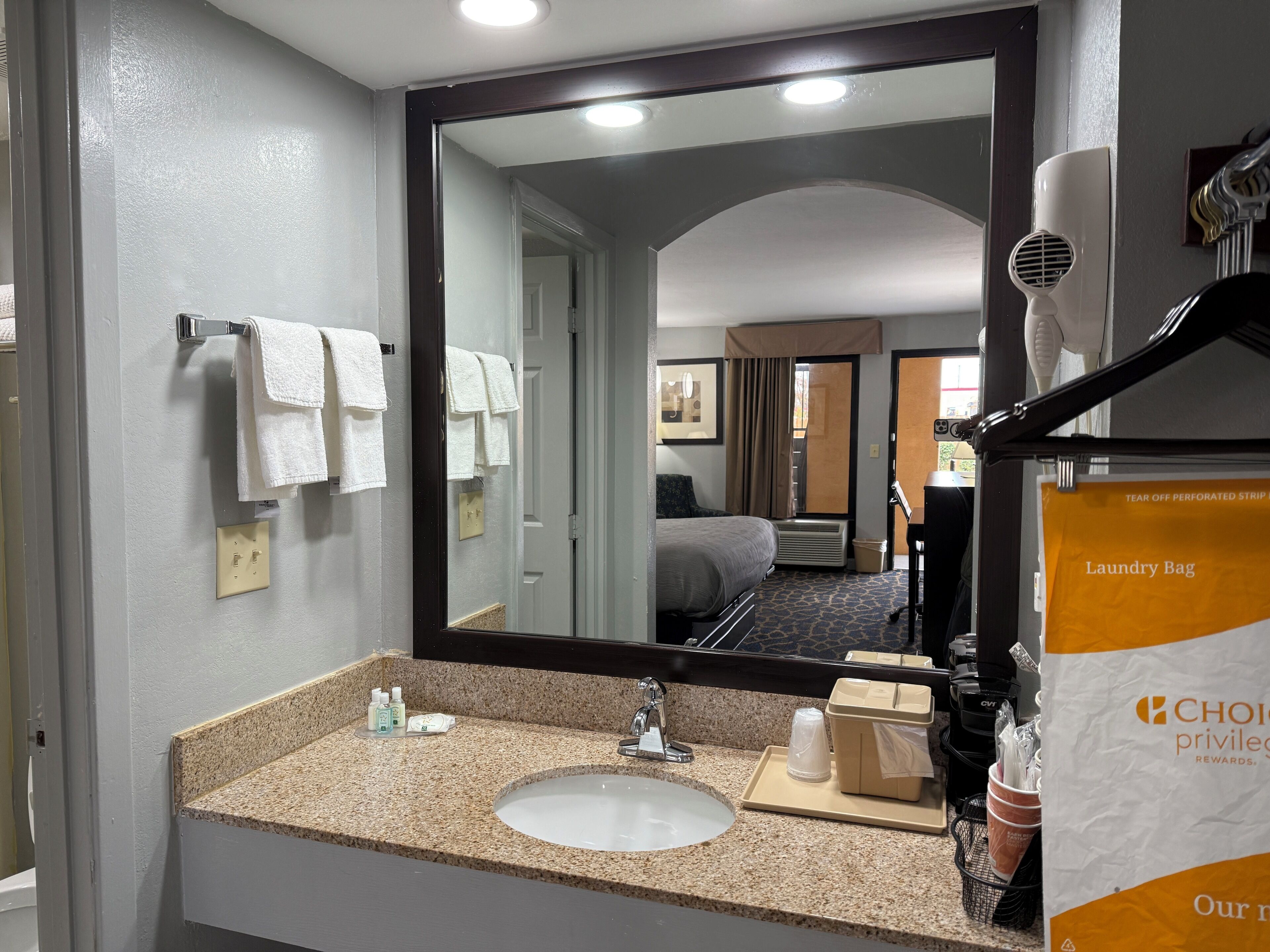 Un baño de hotel con lavamanos, espejo, toallero y secador de pelo.