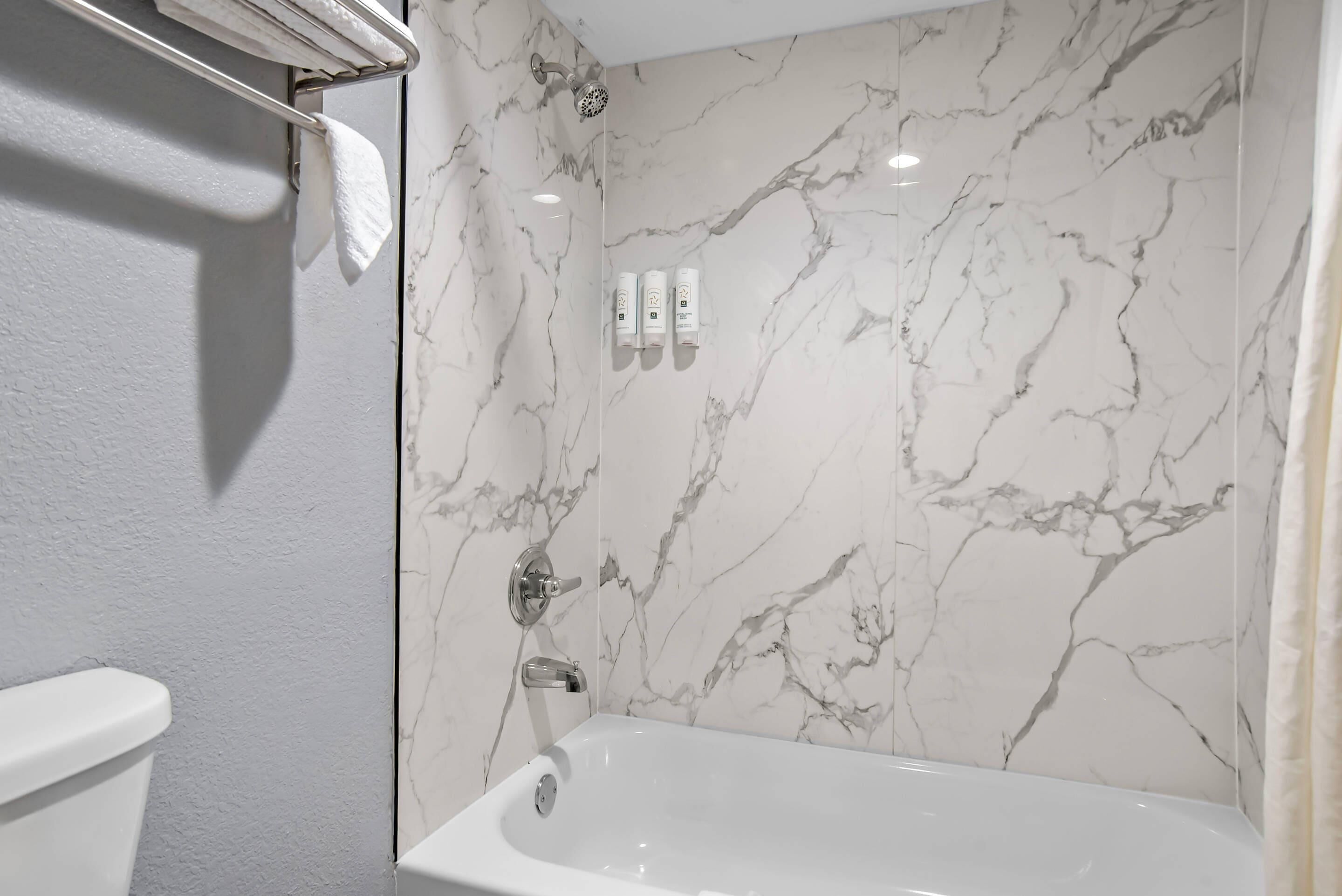 A bathroom with a white bathtub, a shower, and marble walls.