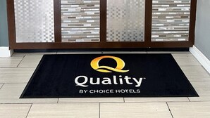 Mostrador de recepción de hotel con una pantalla digital, un reloj y un cartel que dice "Quality by Choice Hotels".