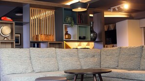 Una sala de estar moderna con un sofá seccional gris, una mesa de centro redonda y una estantería con diversos objetos decorativos.