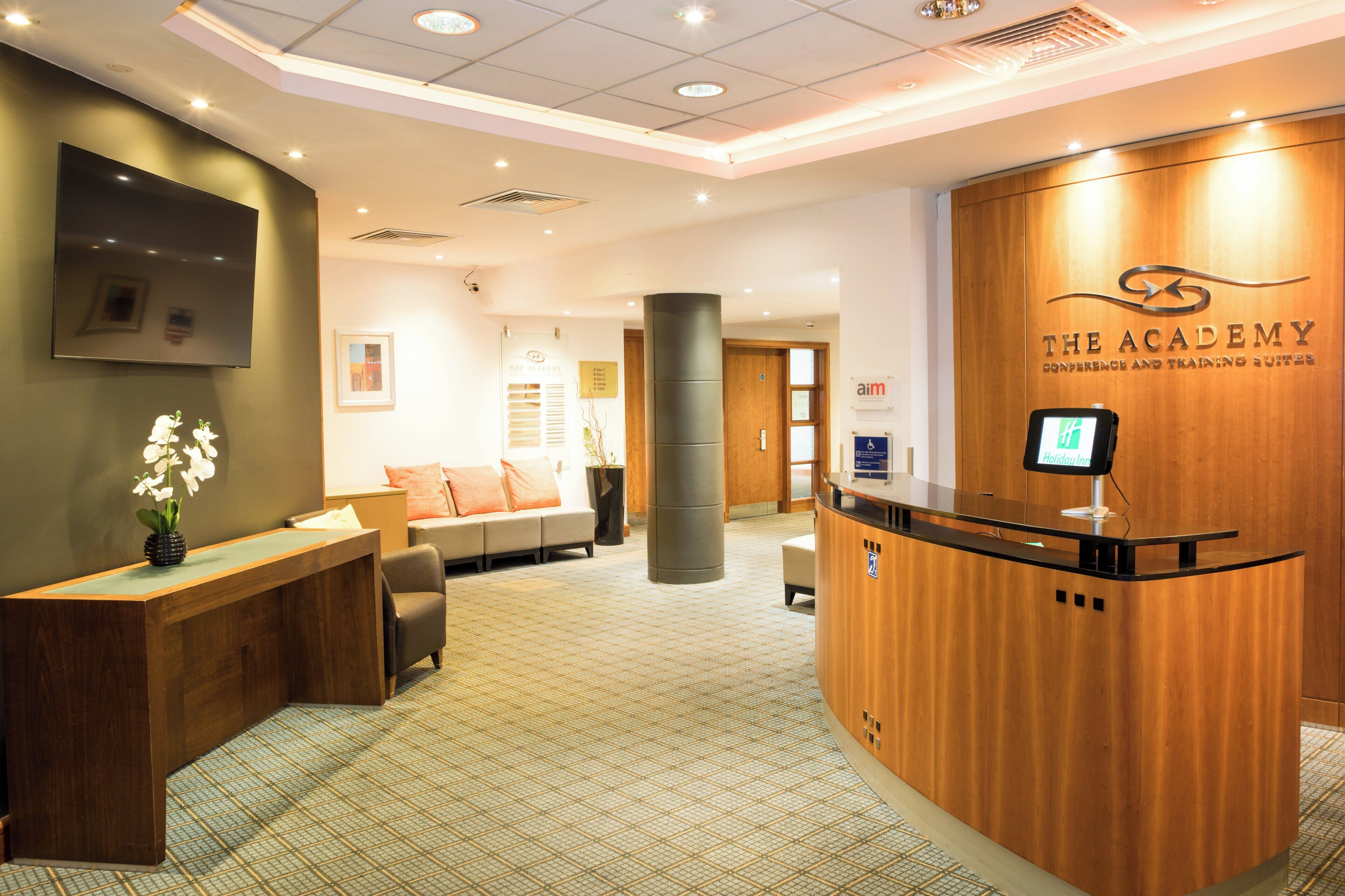 A reception area with a wooden reception desk, a sofa, and a TV mounted on the wall.