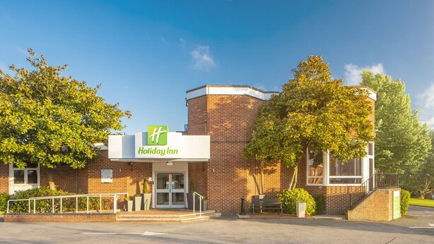 Un hotel Holiday Inn con fachada de ladrillo, entrada de vidrio y logotipo verde.