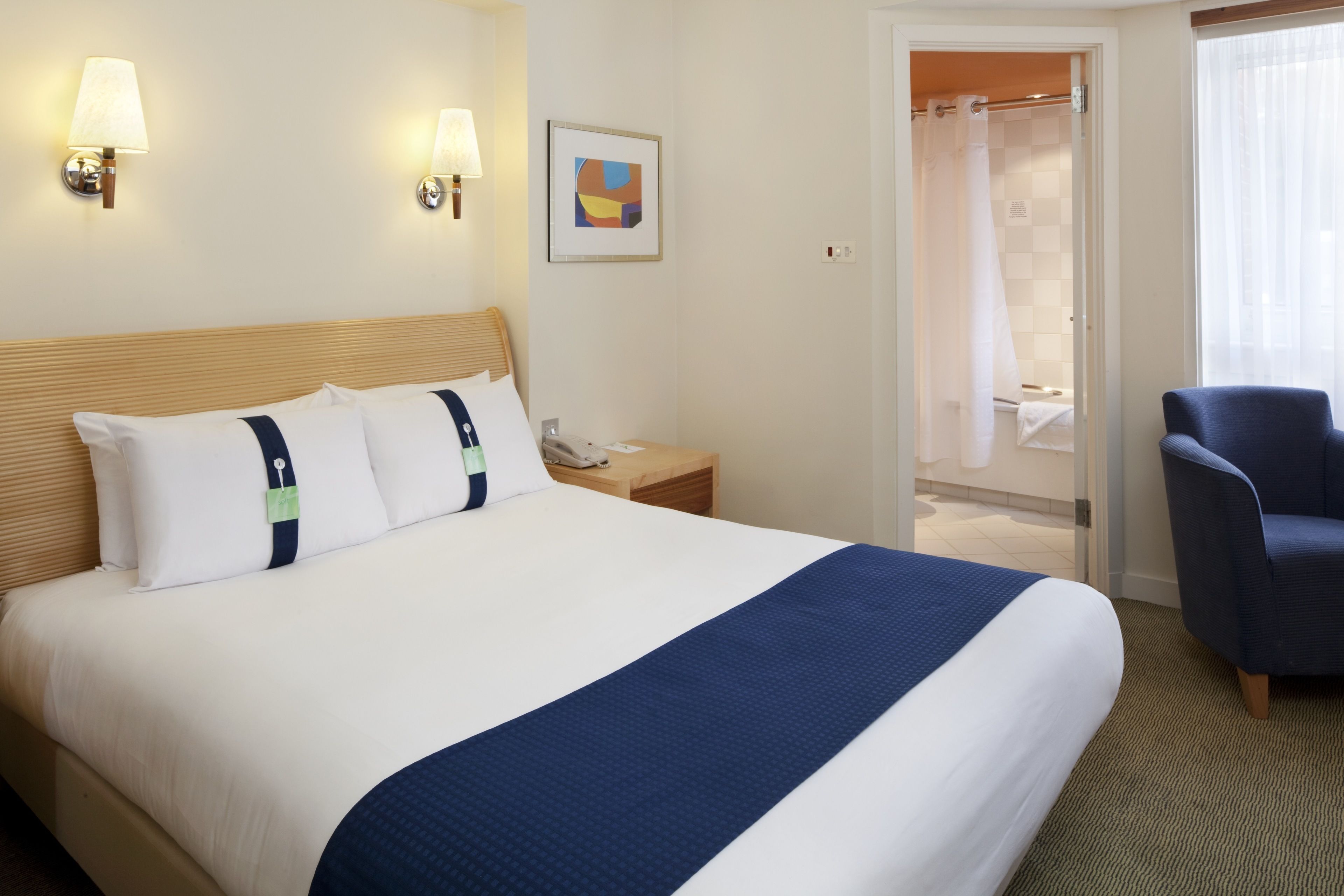 A hotel room with a large bed, bedside tables, a chair, and a shower area.