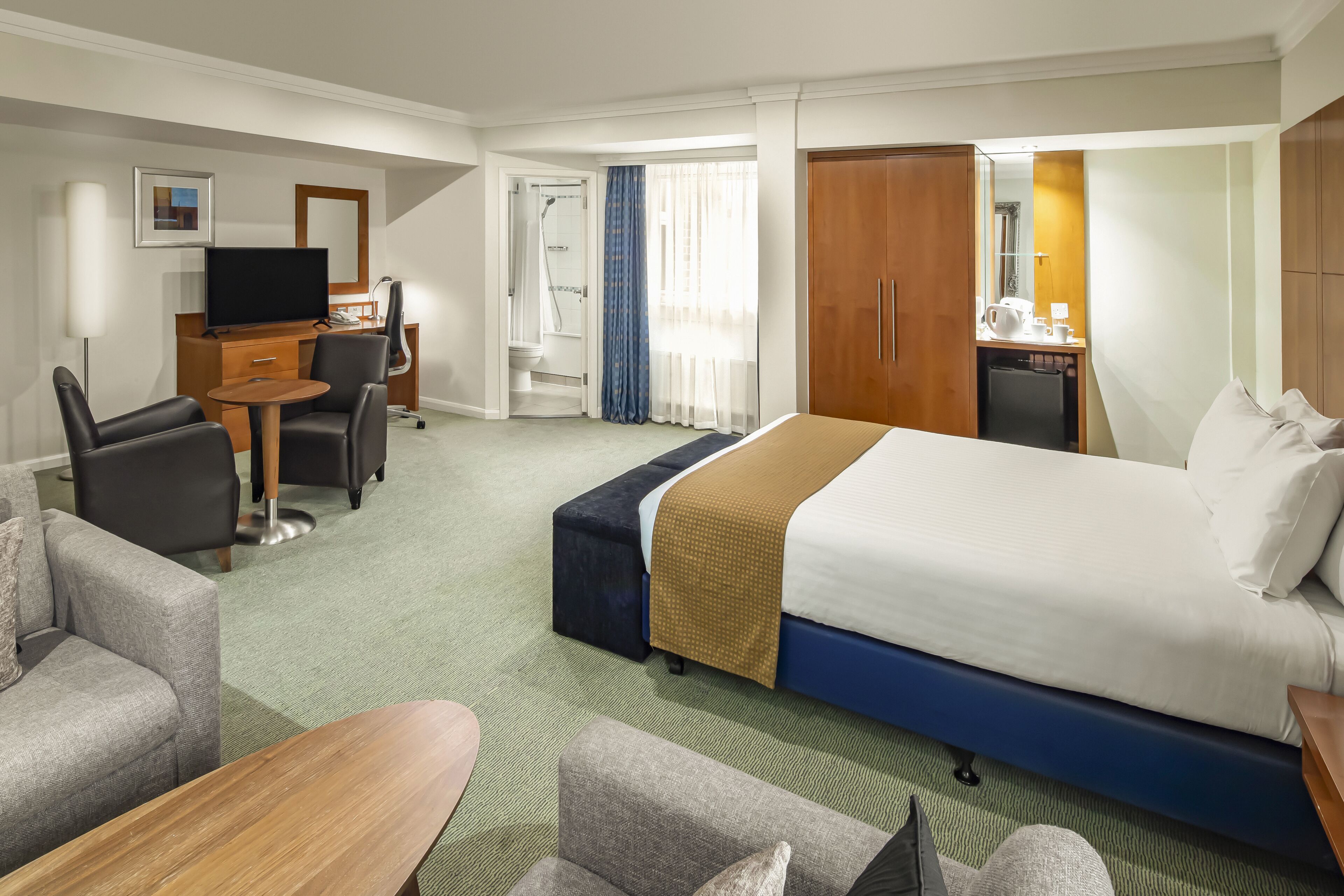 Une chambre d’hôtel avec un lit, un bureau et une chaise, une télévision et une salle de bain visible à travers une porte ouverte.
