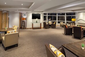 A hotel lobby with seating areas, a Starbucks sign, a large window with a city view, and a flat-screen TV mounted on the wall. - Holiday Inn Basingstoke by IHG (Basingstoke)