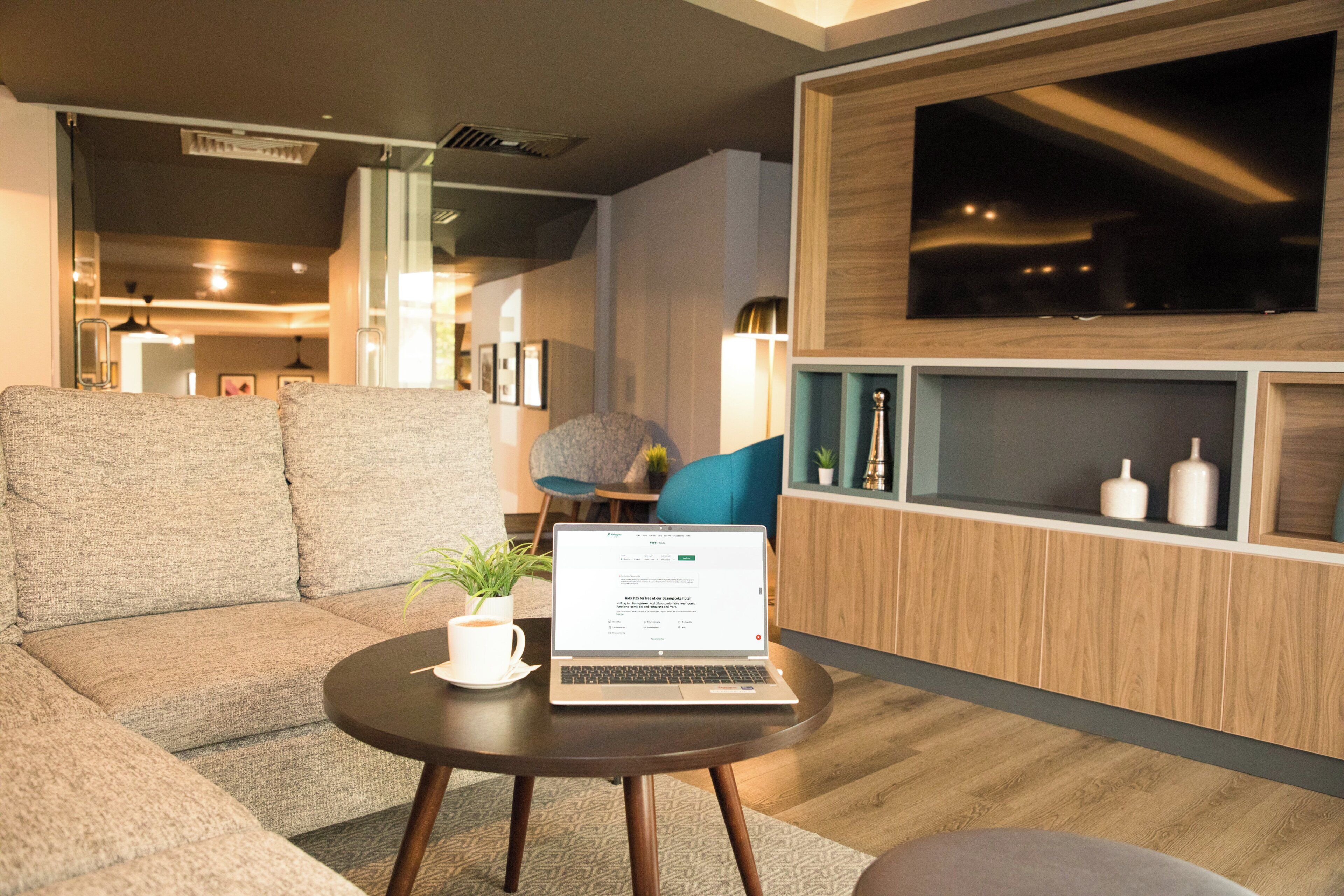 A modern living room with a sofa, a round table with a laptop, and a TV mounted on the wall.