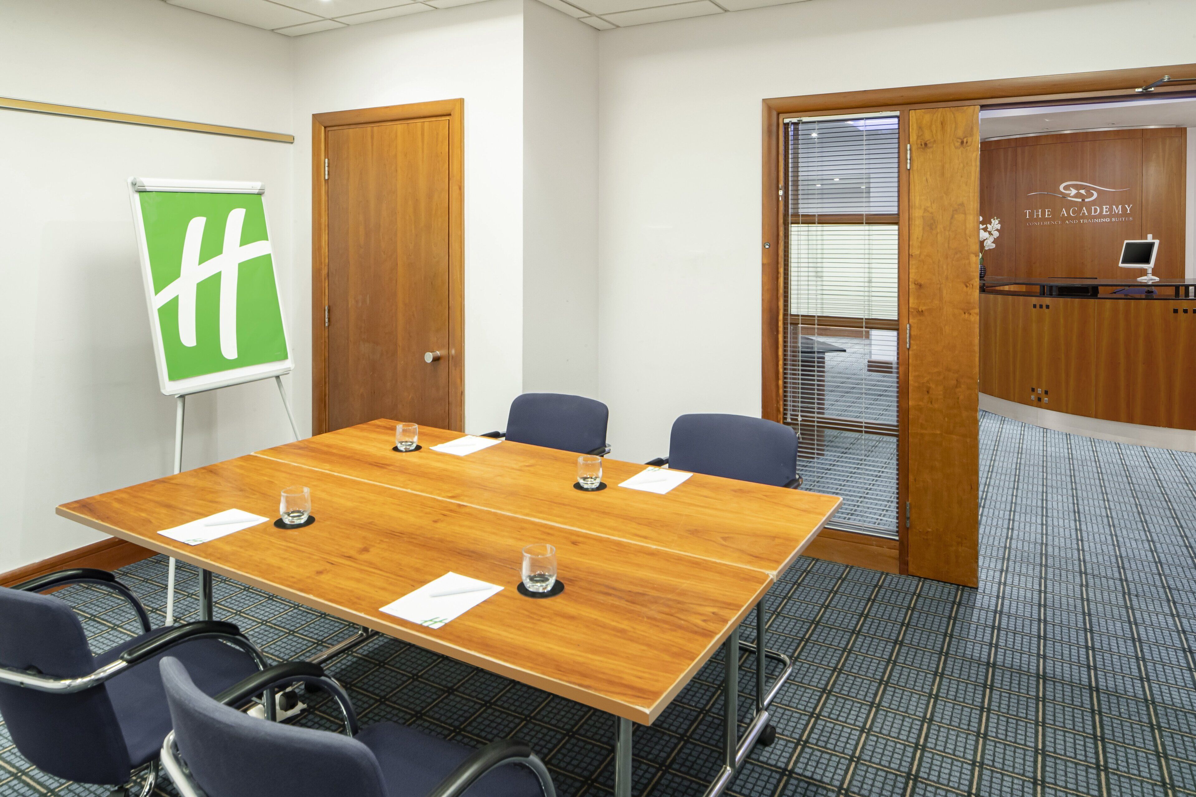 Un salón de conferencias con una mesa de madera, seis sillas, un rotafolio y un mostrador de recepción.