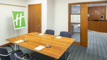 Un salón de conferencias con una mesa de madera, seis sillas, un rotafolio y un mostrador de recepción.