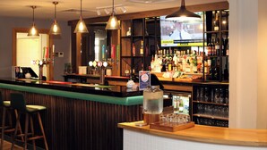 Zona de bar con mostrador, taburetes, una pantalla de televisión y estantes llenos de botellas.