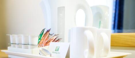 A tray with a set of white mugs, a spoon, and a card labeled "Holiday Inn" on a wooden table.