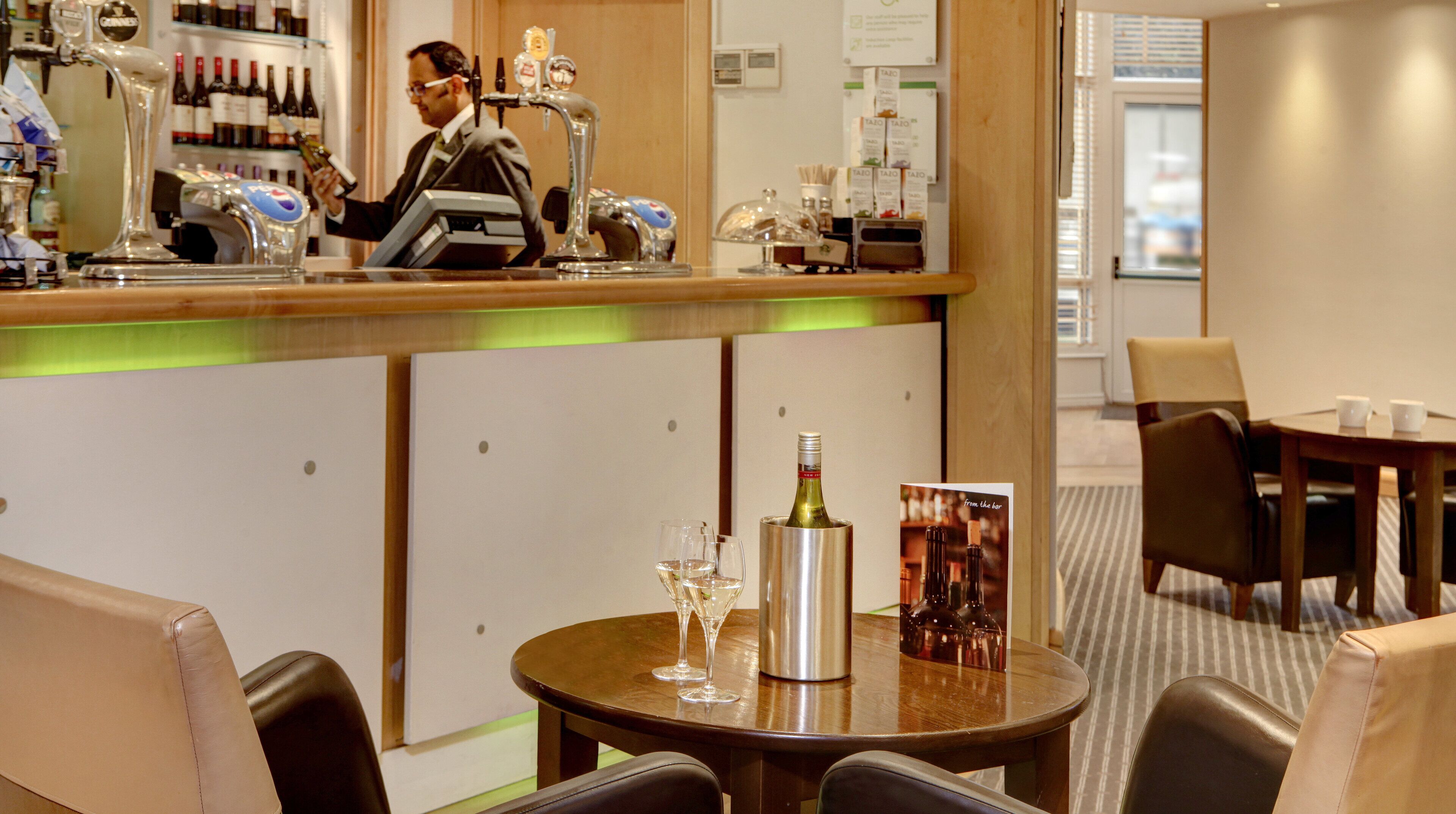 A bar area with a bartender, a bottle of wine, and glasses on a table.