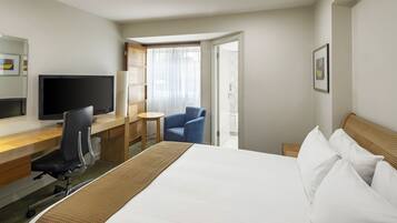 A hotel room with a bed, a desk with a chair, a television, and a window with curtains.