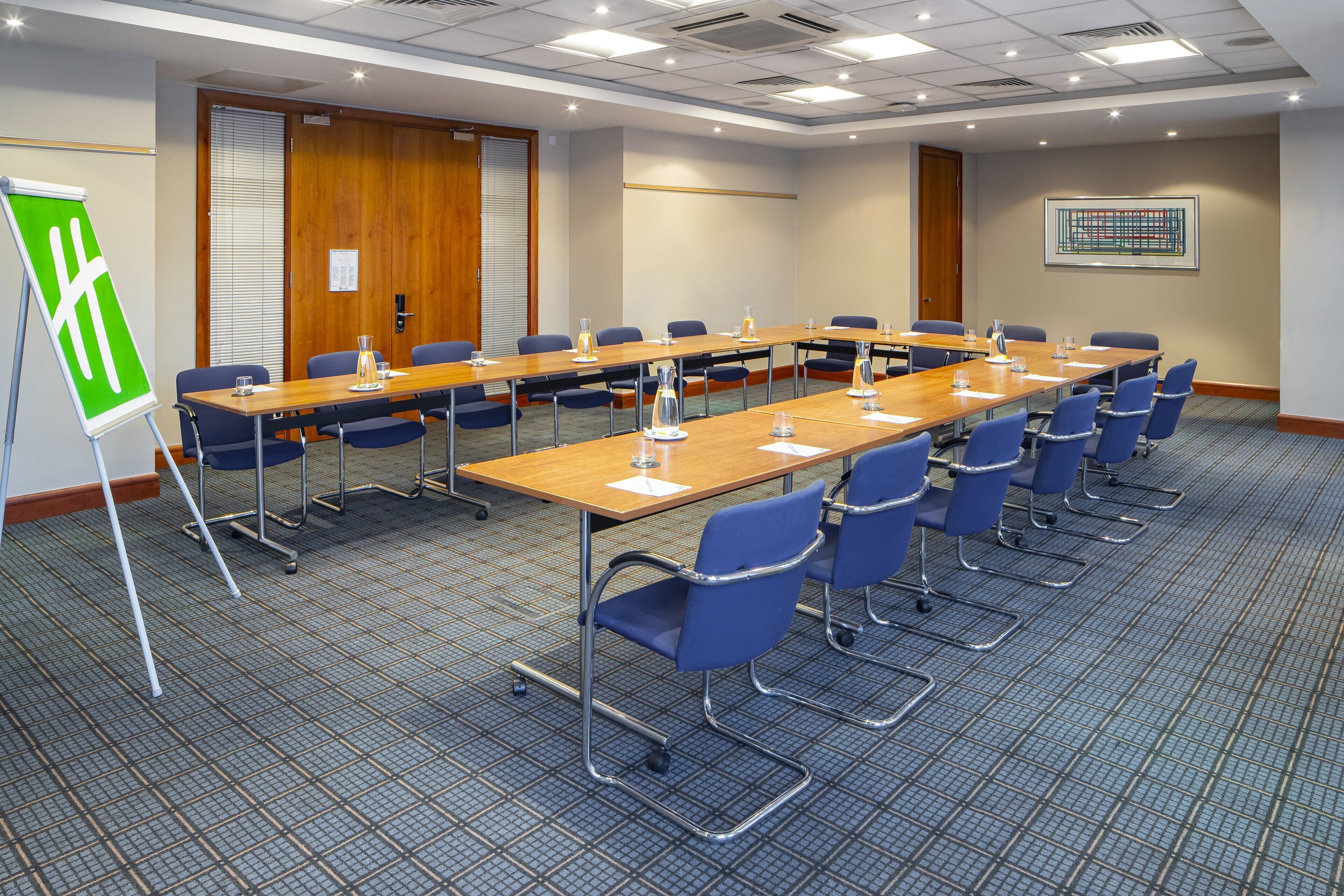 A conference room with a long table, blue chairs, and a green directional sign.