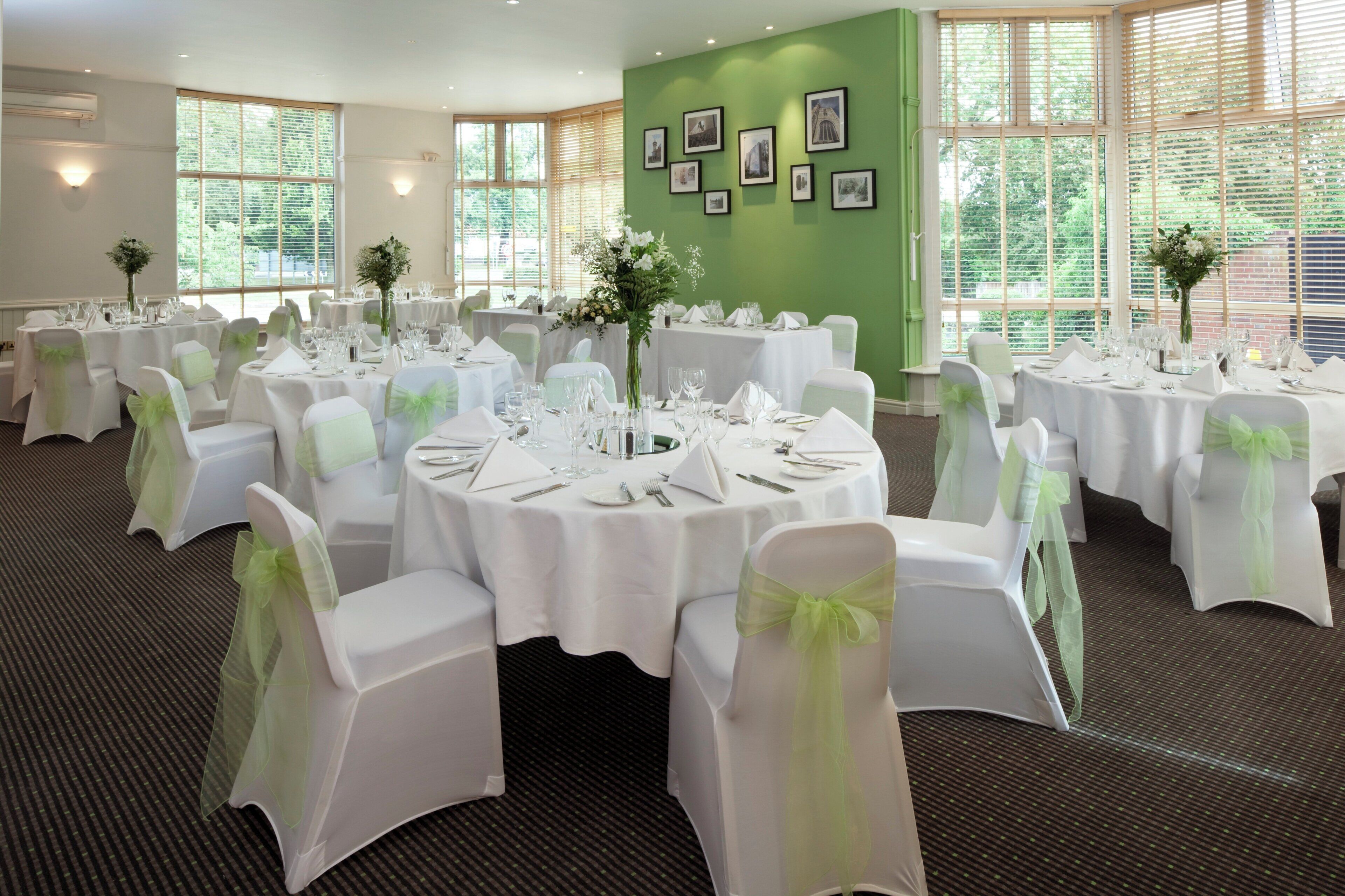 Un salón de banquetes con mesas redondas, manteles blancos y sillas con cintas verdes.