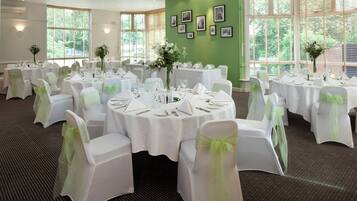 Un salón de banquetes con mesas redondas, manteles blancos y sillas con cintas verdes.