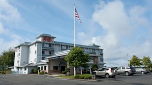A hotel with a flagpole, a parking lot, and a clear sky. - Shilo Inn Suites Warrenton (Warrenton)