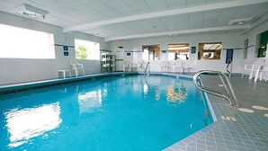 Una piscina interior con agua cristalina, suelo de baldosas y sillas blancas alrededor.
