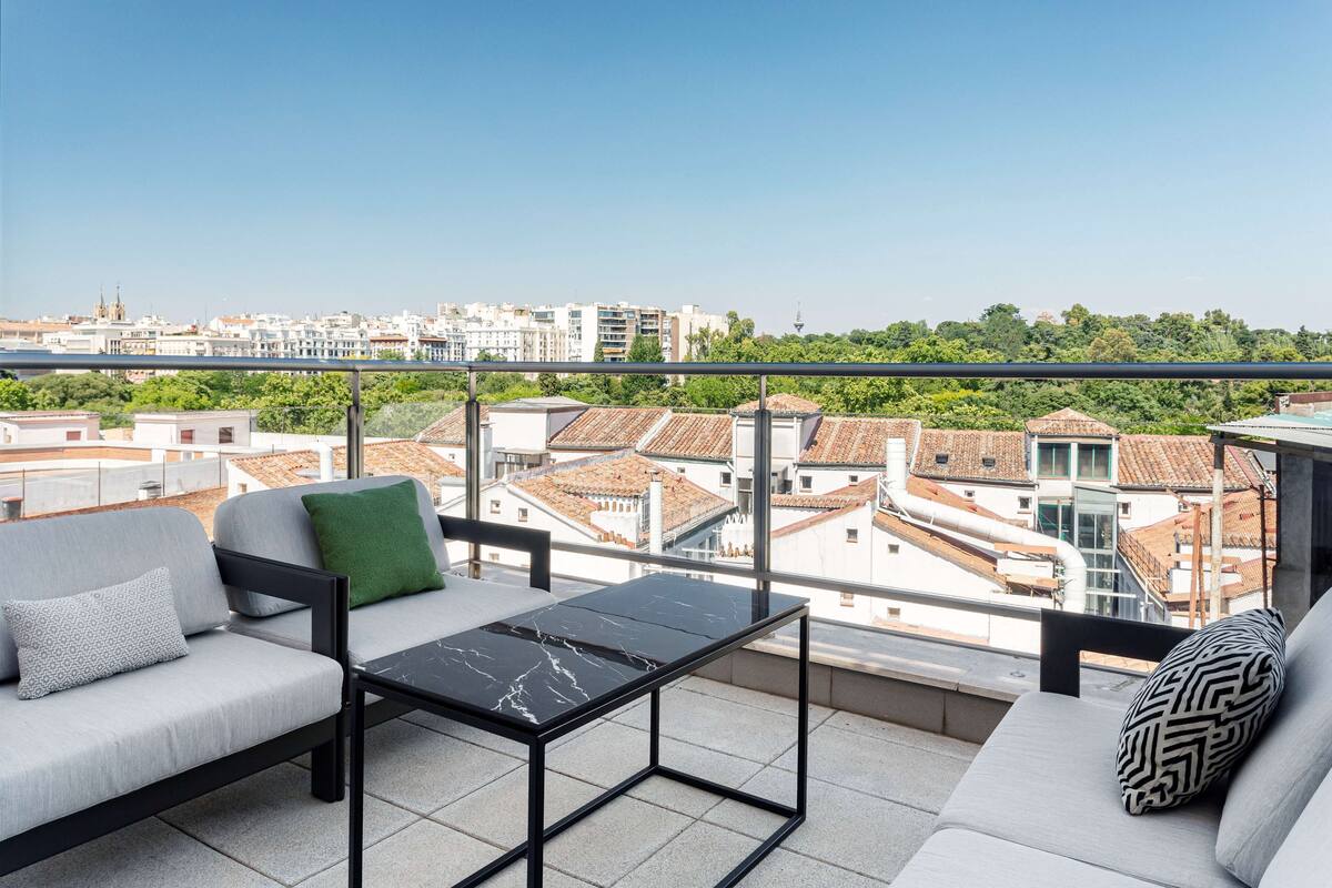 Een balkon met een bank, een tafeltje en uitzicht op de stad.