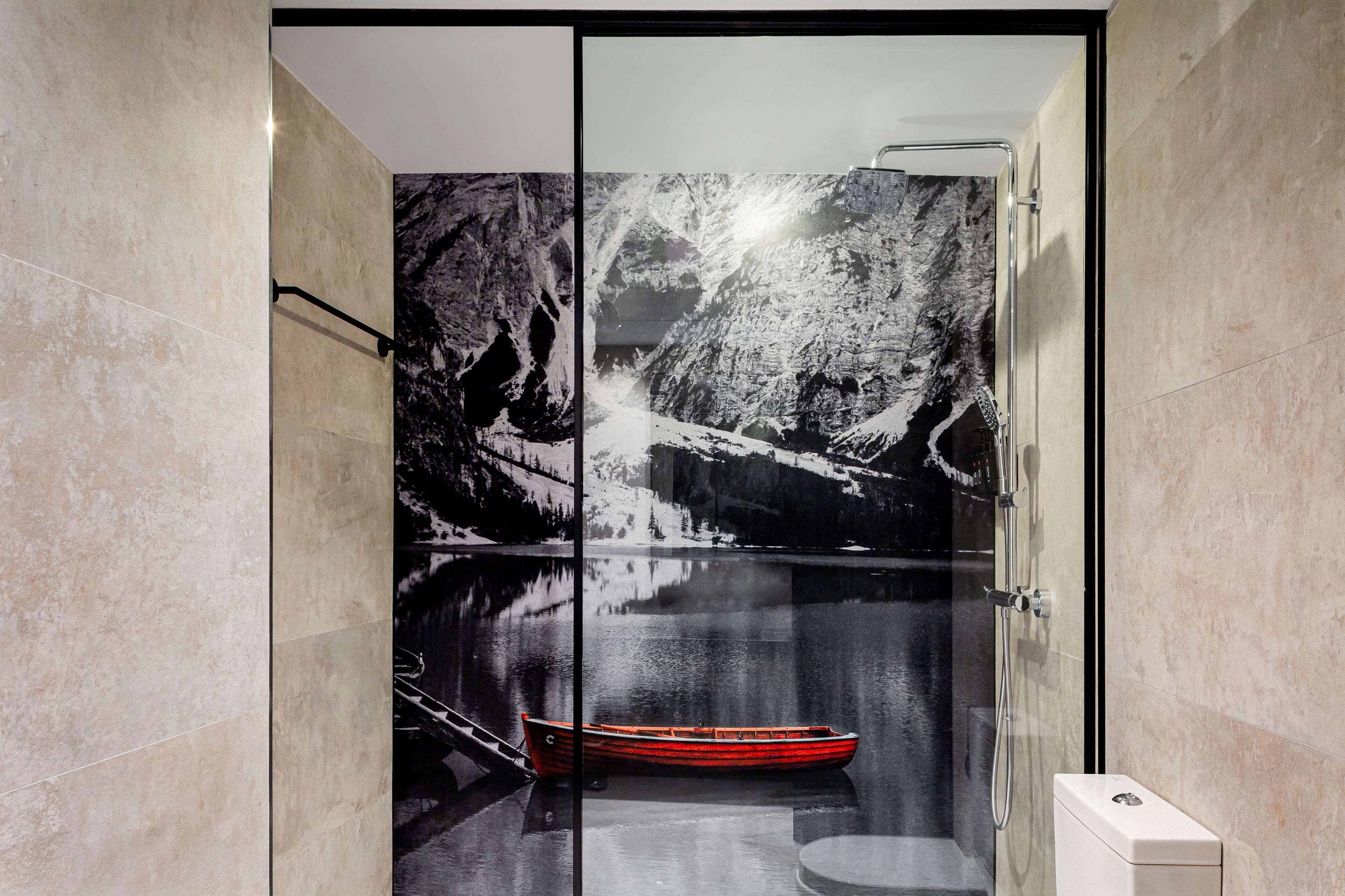 A bathroom with a glass shower enclosure, a red boat in the background, and a white toilet.