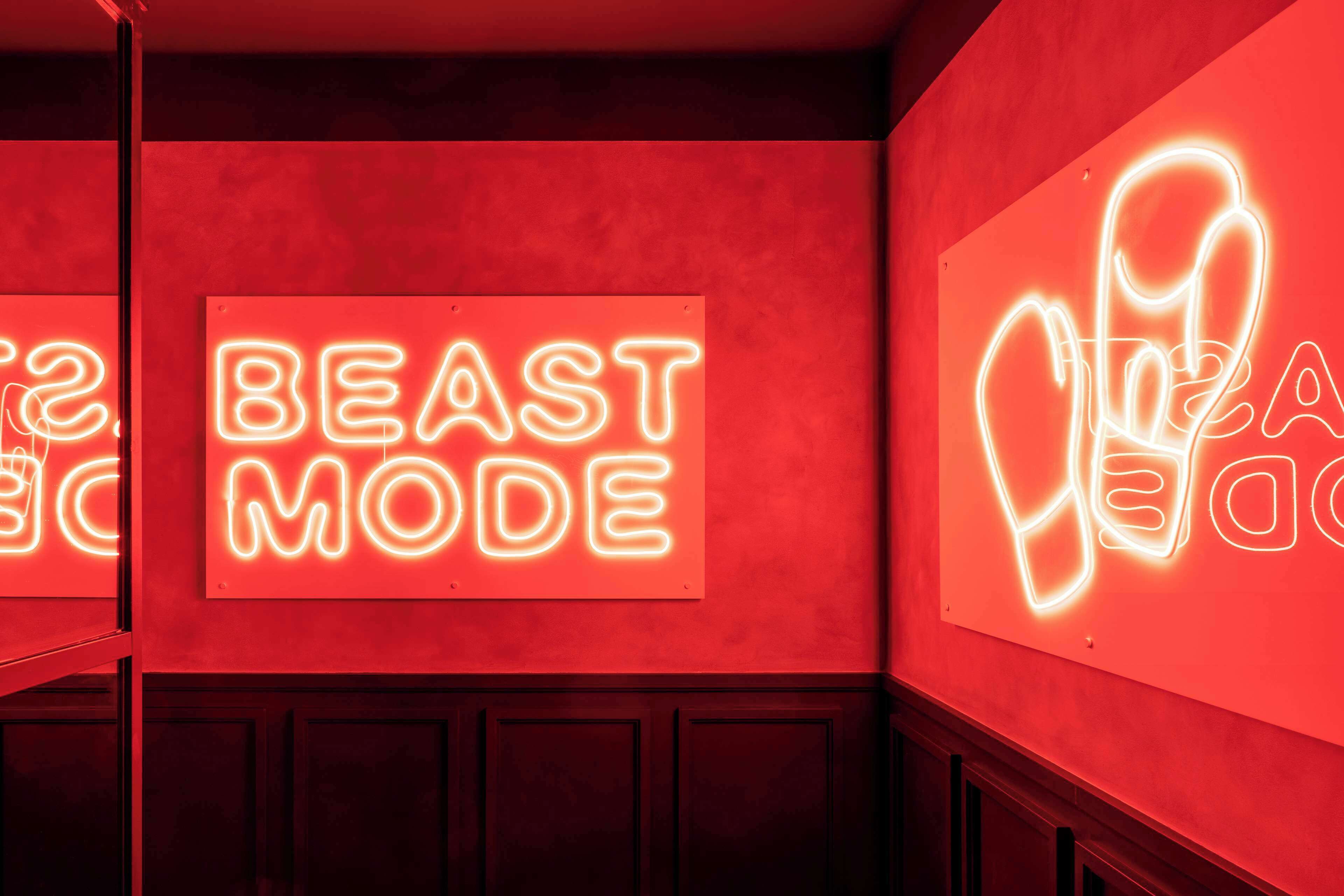 A neon sign with the words "BEAST MODE" on a red wall.