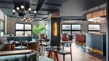 Un espace lounge moderne avec des sièges confortables, un bar et de grandes fenêtres offrant une vue sur la ville.