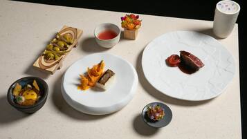 A table with various dishes, including a bowl of soup, a plate with a piece of meat, and a small dish with vegetables.