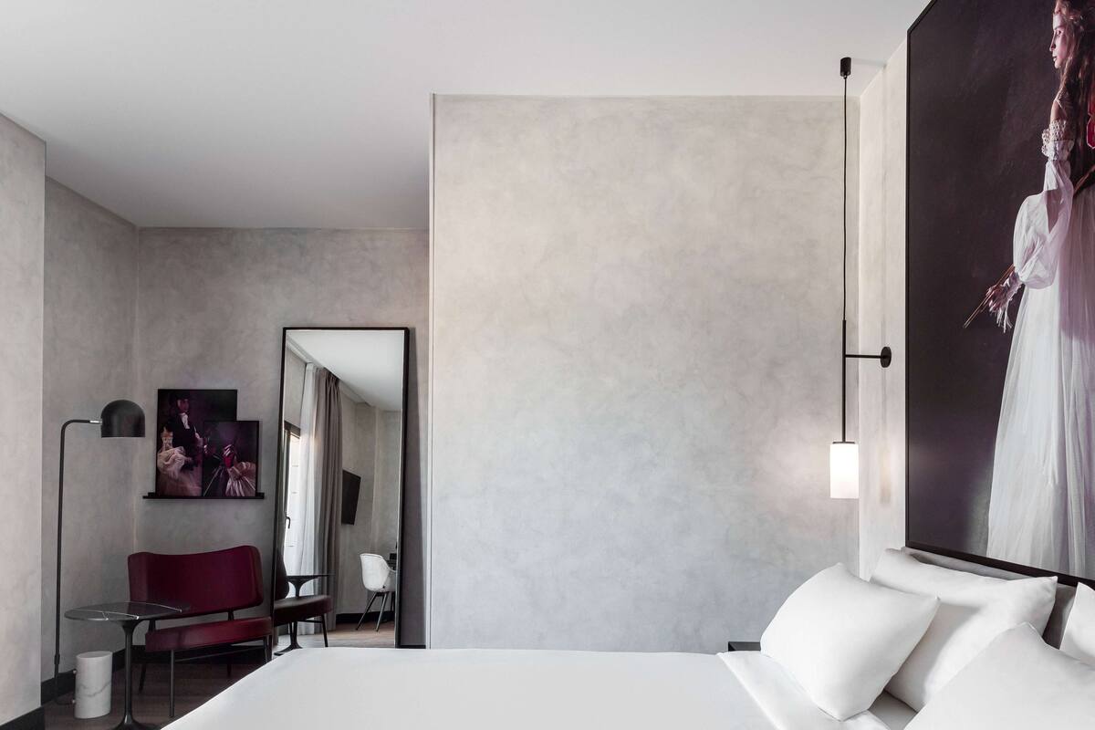 Een moderne hotelkamer met een groot bed, een rode stoel, een klein tafeltje en een schilderij aan de muur.